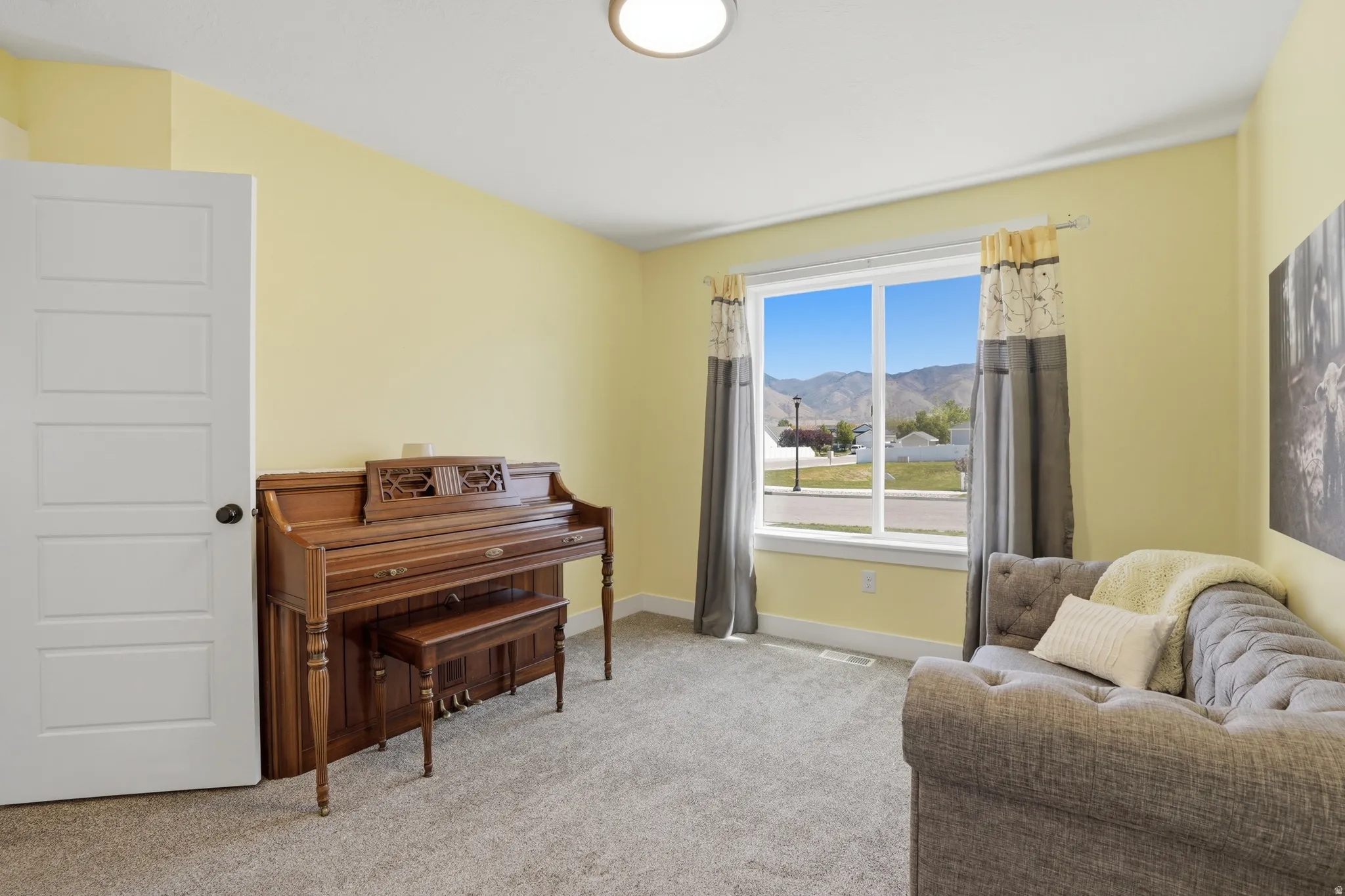 Bright bedroom with light yellow walls, a single-panel interior door, and a large window providing natural light