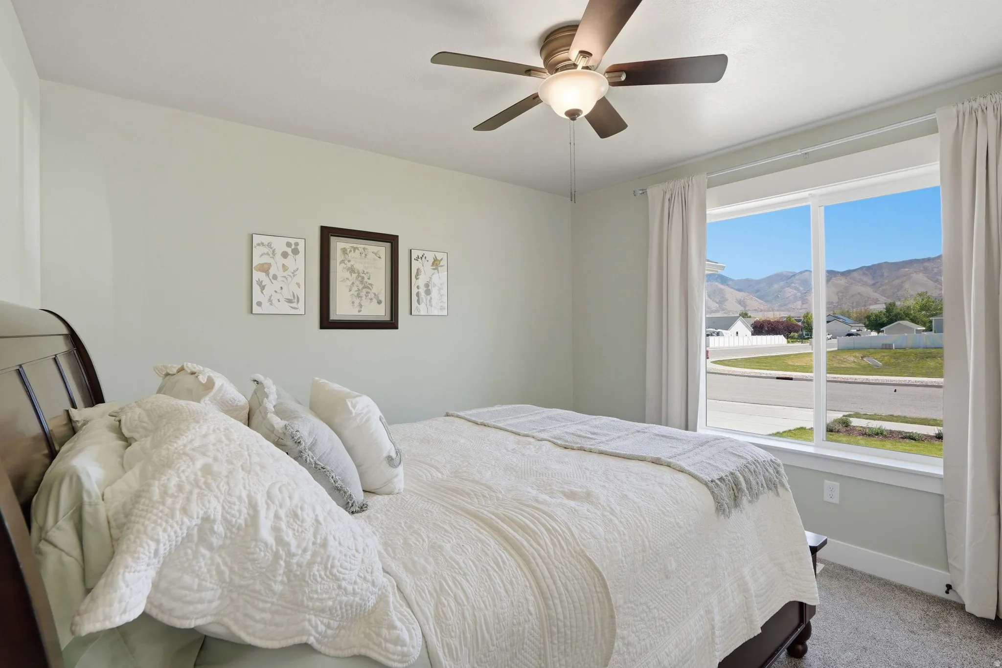 Bedroom featuring a large window with mountain scenery, a ceiling fan with integrated lighting, light-colored walls, and carpeting