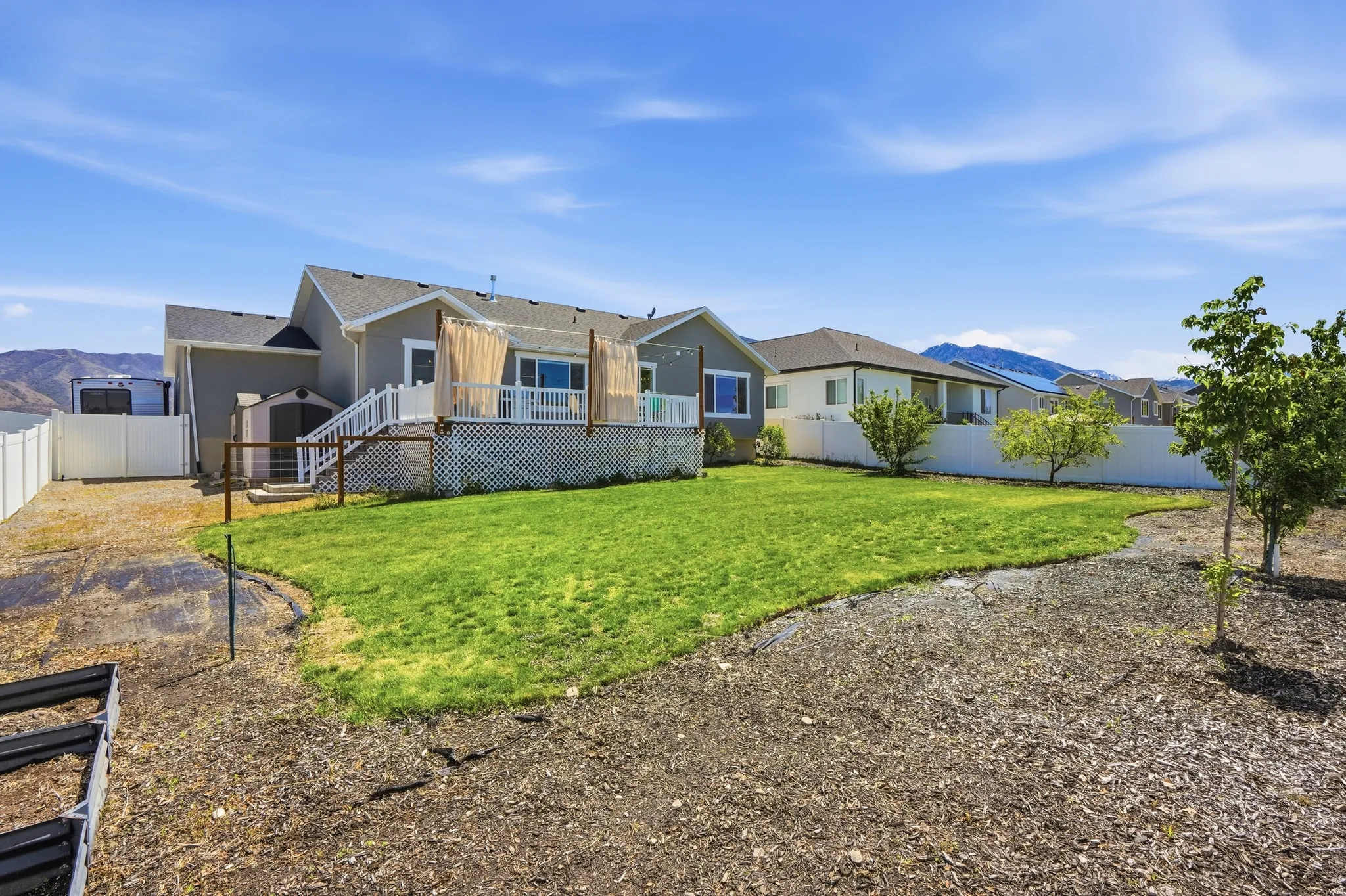Expansive backyard featuring lawn, garden boxes  a large deck with white railings, and a gravel perimeter