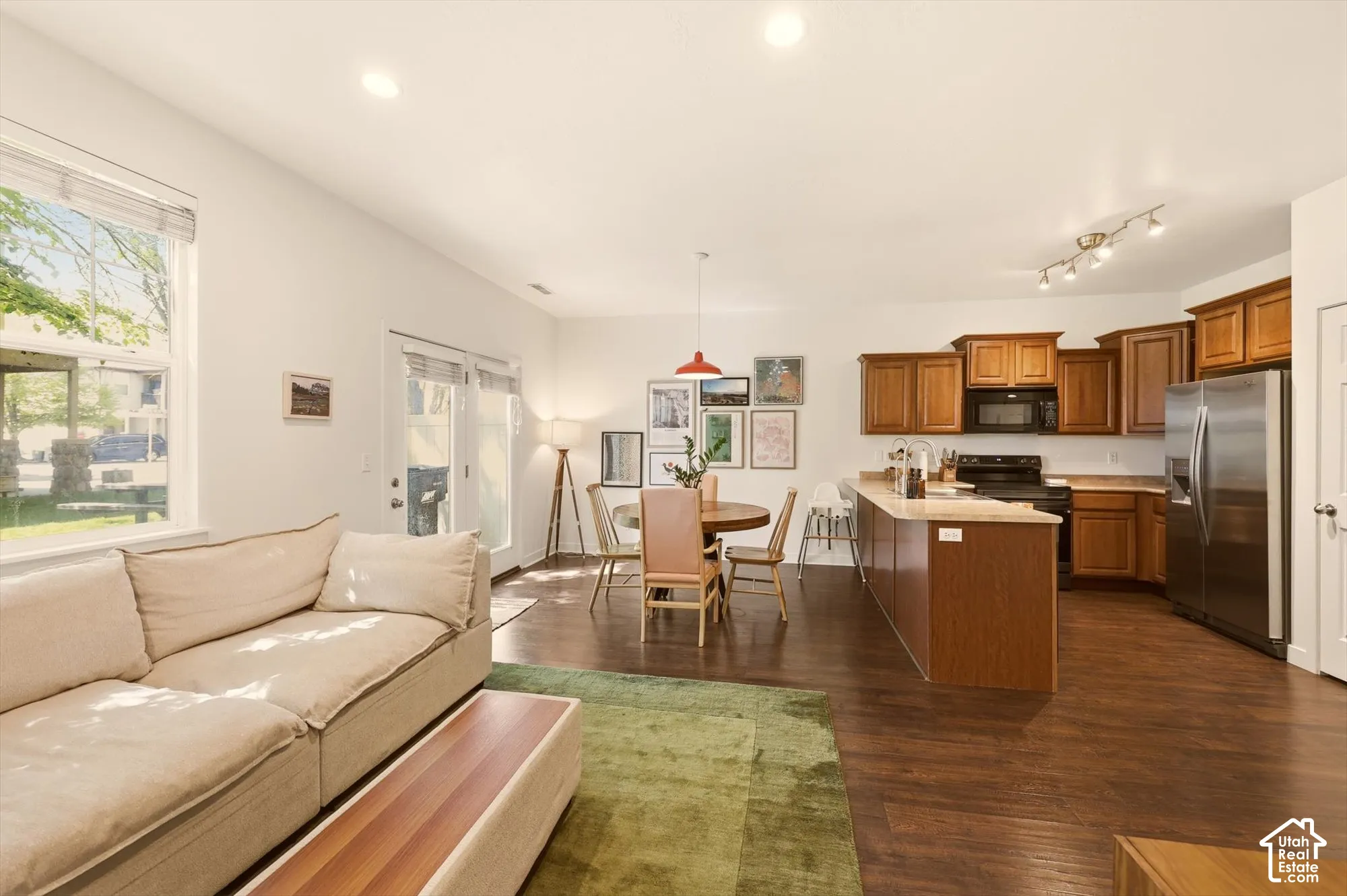 Open-concept living area featuring wood-finish flooring, recessed lighting, and a kitchen with wood cabinetry, stainless steel refrigerator, and a kitchen island with seating