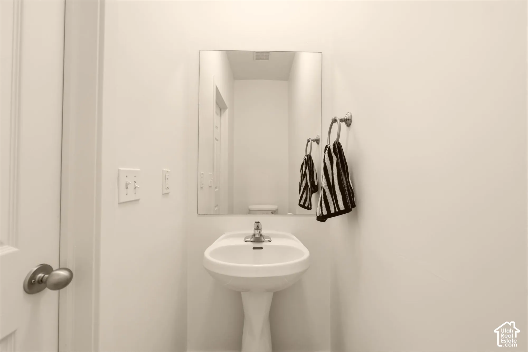 Pedestal sink featuring a chrome faucet, rectangular wall-mounted mirror, and wall-mounted towel ring