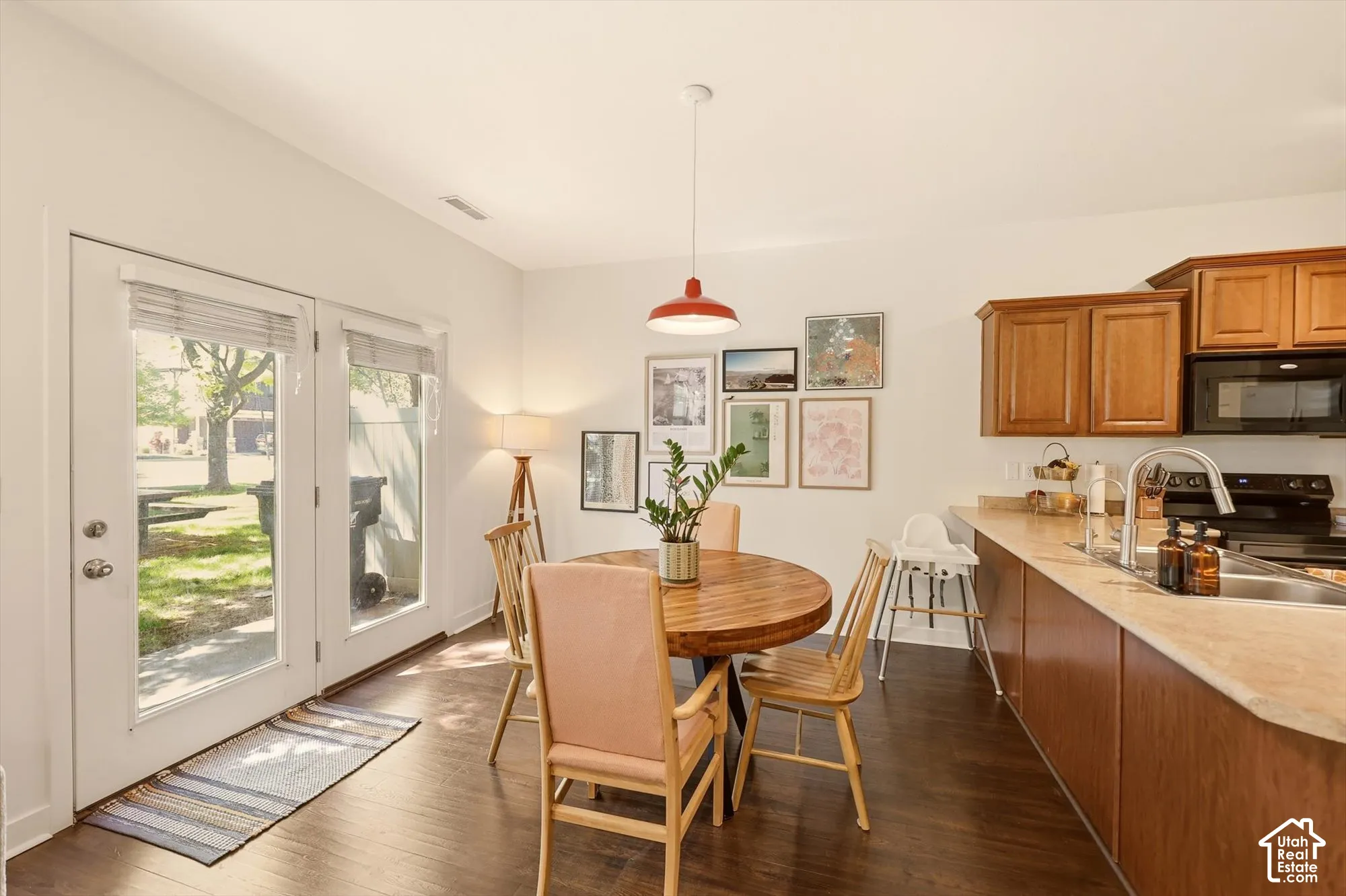 Open-concept kitchen and dining area featuring wood-finish flooring, warm wood cabinetry, a stainless steel sink with a modern faucet, and a dual glass-paneled door entry to the exterior