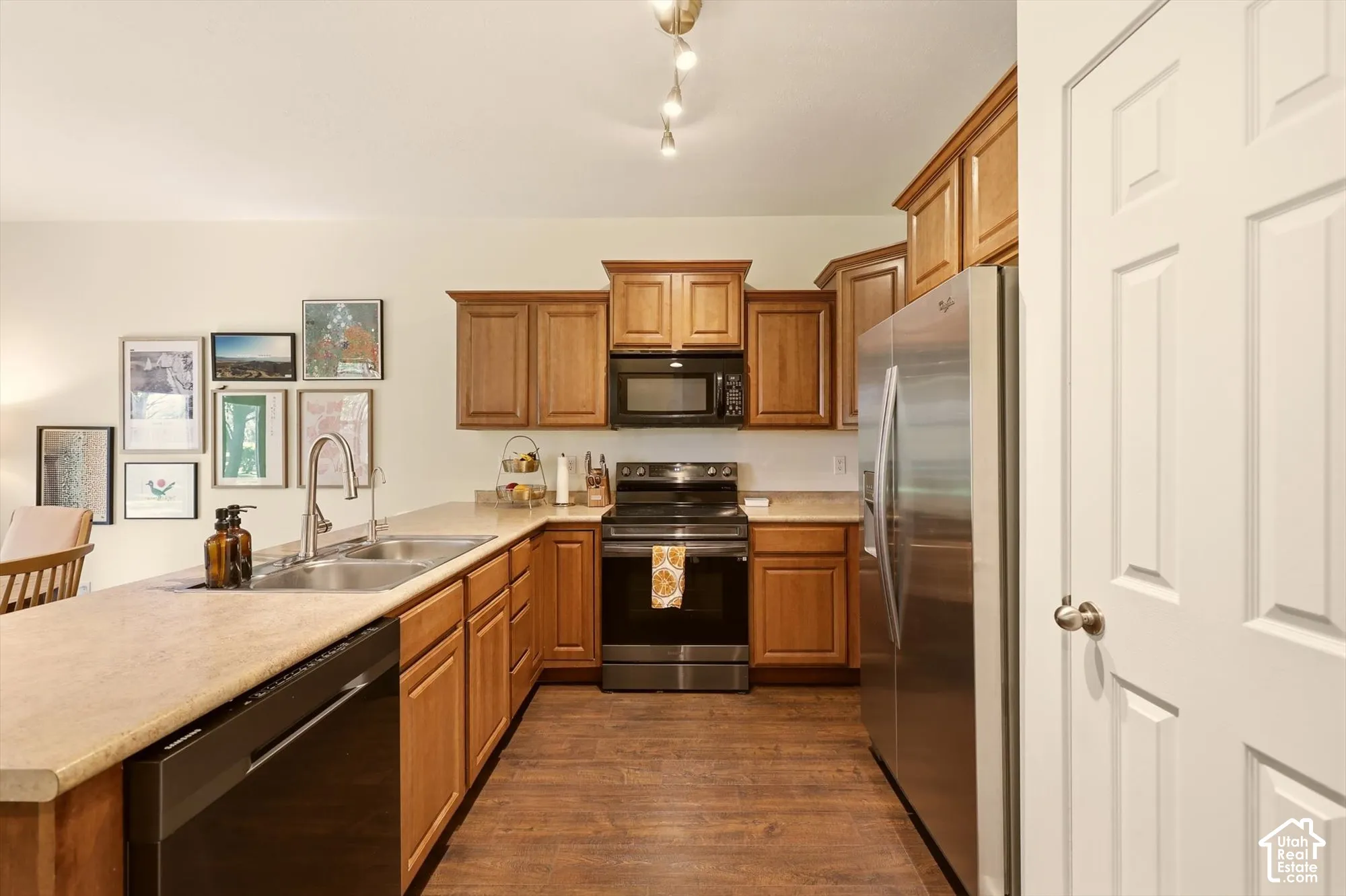 Kitchen featuring wood-finish flooring, light-colored countertops, stainless steel refrigerator, black range, and wood cabinetry