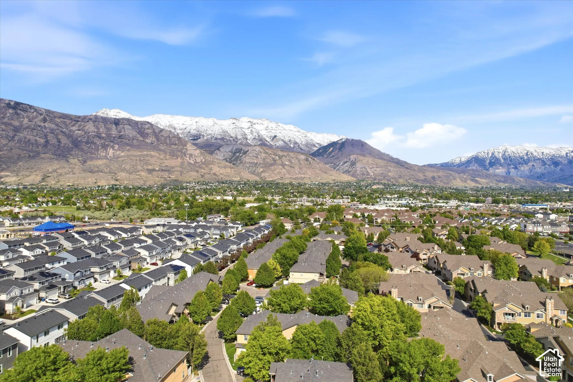 Expansive residential neighborhood featuring diverse housing styles, mature trees, and mountainous terrain with snow-capped peaks in the distance