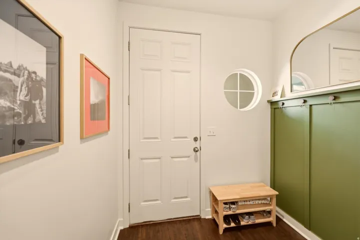 Entryway featuring a white paneled door, circular window, built-in green accent paneling, and wood-finish flooring