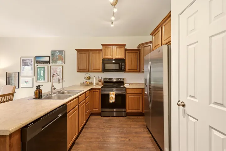 Kitchen featuring wood-finish flooring, light-colored countertops, stainless steel refrigerator, black range, and wood cabinetry