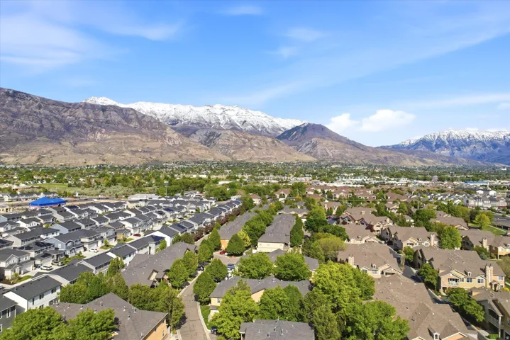 Expansive residential neighborhood featuring diverse housing styles, mature trees, and mountainous terrain with snow-capped peaks in the distance