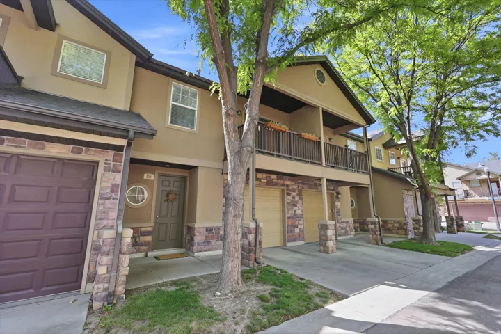 Multi-level facade featuring stone veneer accents, an inviting entryway, a private balcony, an attached garage, and mature landscaping