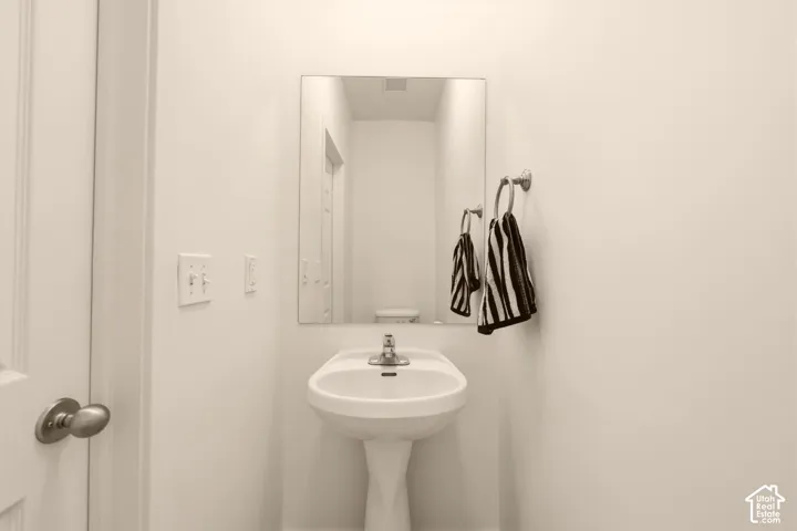 Pedestal sink featuring a chrome faucet, rectangular wall-mounted mirror, and wall-mounted towel ring
