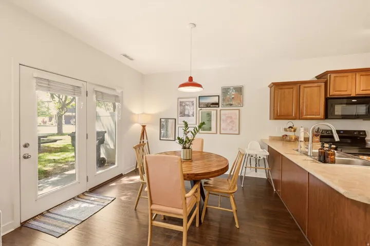 Open-concept kitchen and dining area featuring wood-finish flooring, warm wood cabinetry, a stainless steel sink with a modern faucet, and a dual glass-paneled door entry to the exterior