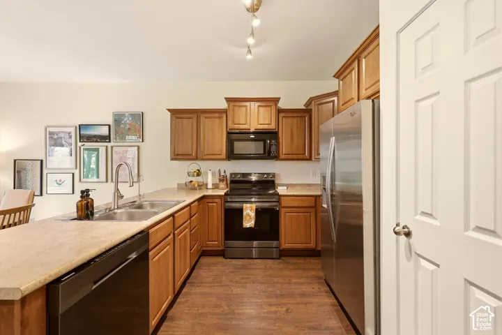 Kitchen featuring wood-finish flooring, light-colored countertops, stainless steel refrigerator, black range, and wood cabinetry