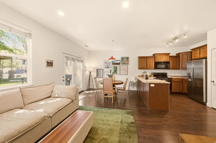 Open-concept living area featuring wood-finish flooring, recessed lighting, and a kitchen with wood cabinetry, stainless steel refrigerator, and a kitchen island with seating