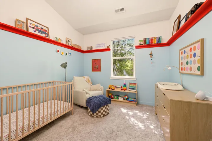 Vaulted ceiling room featuring a large window, light blue wall paneling with a red accent trim, and neutral carpeting