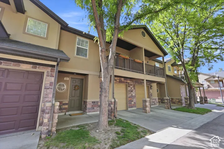 Multi-level facade featuring stone veneer accents, an inviting entryway, a private balcony, an attached garage, and mature landscaping