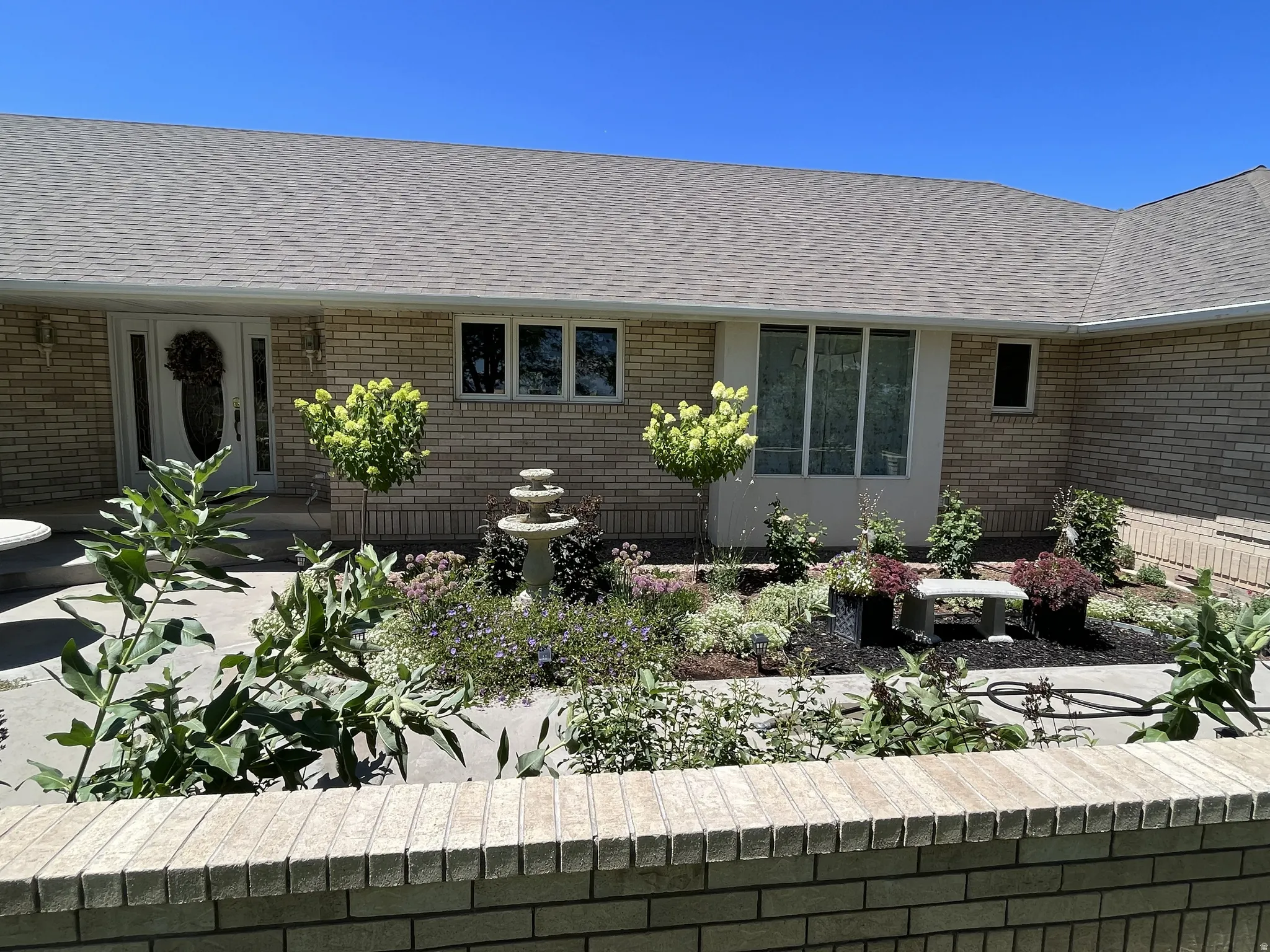 Brick exterior featuring a multi-pane front door with sidelights, a large bay window, and a stone water feature