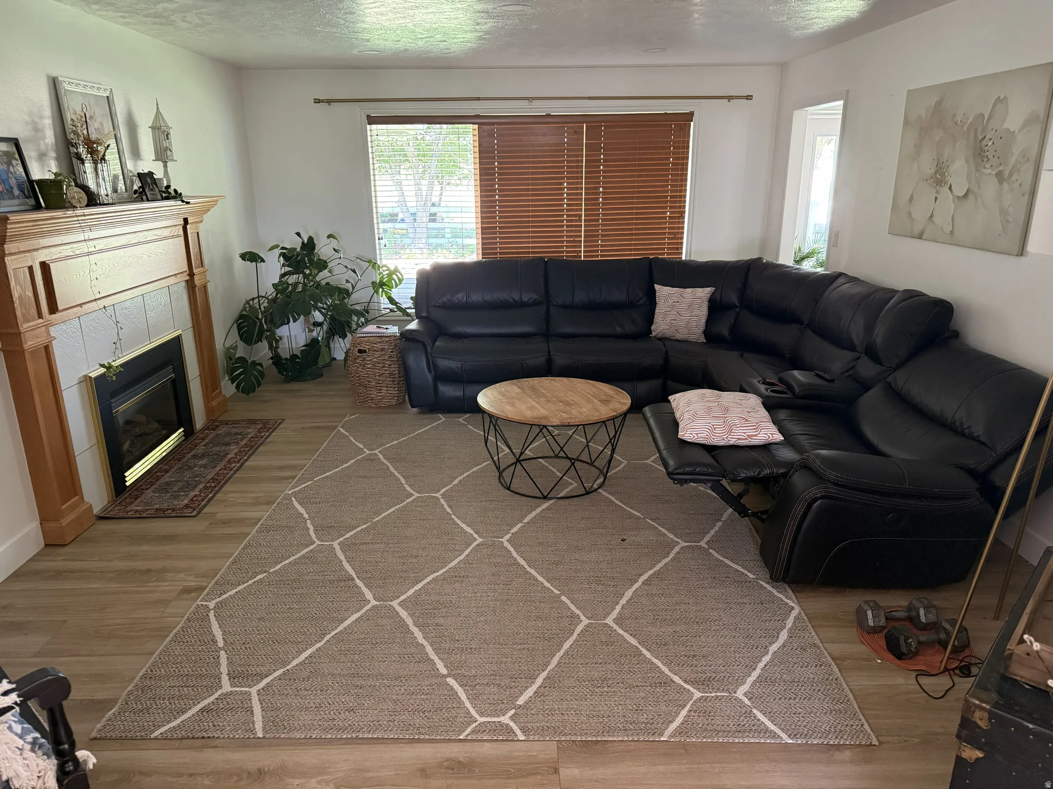 Living space featuring wood-finish flooring, a fireplace with a light-tiled surround, a wood mantel, and window with horizontal blinds