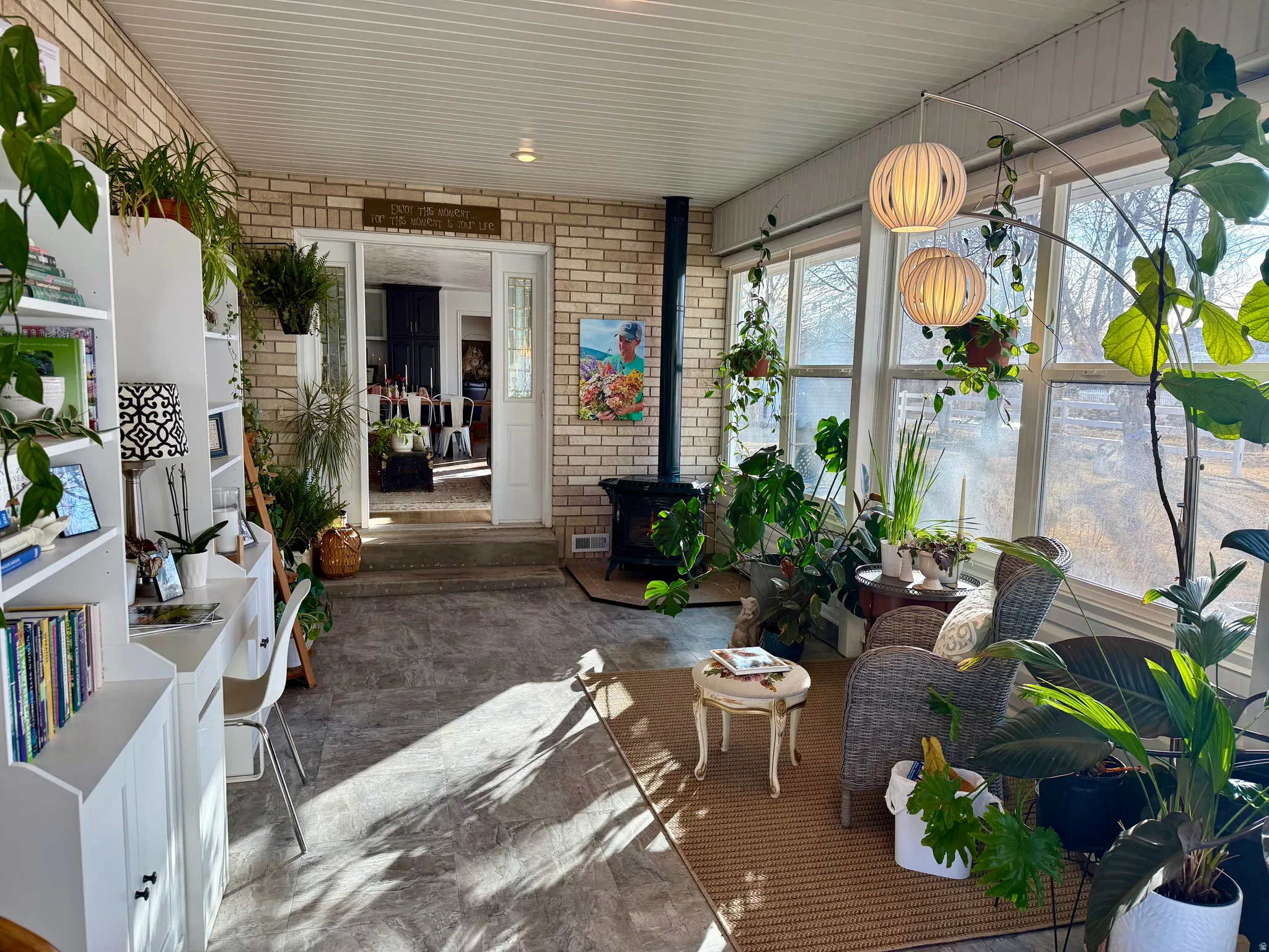 Sun-drenched conservatory featuring extensive window lines, brick accent walls, a wood-burning stove, built-in shelving, and neutral tone flooring