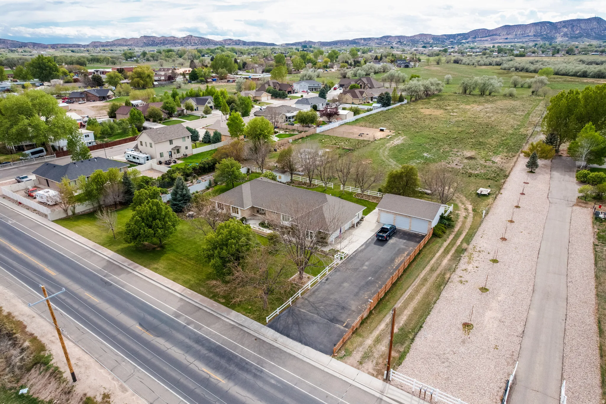Spacious property featuring a single-story residence, a detached three-car garage, an elongated paved driveway, and extensive surrounding land
