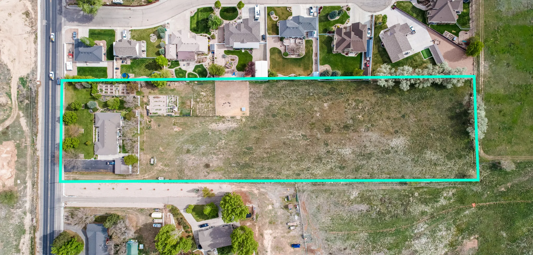 Expansive rectangular parcel featuring a large undeveloped area, existing structures, and mature perimeter trees