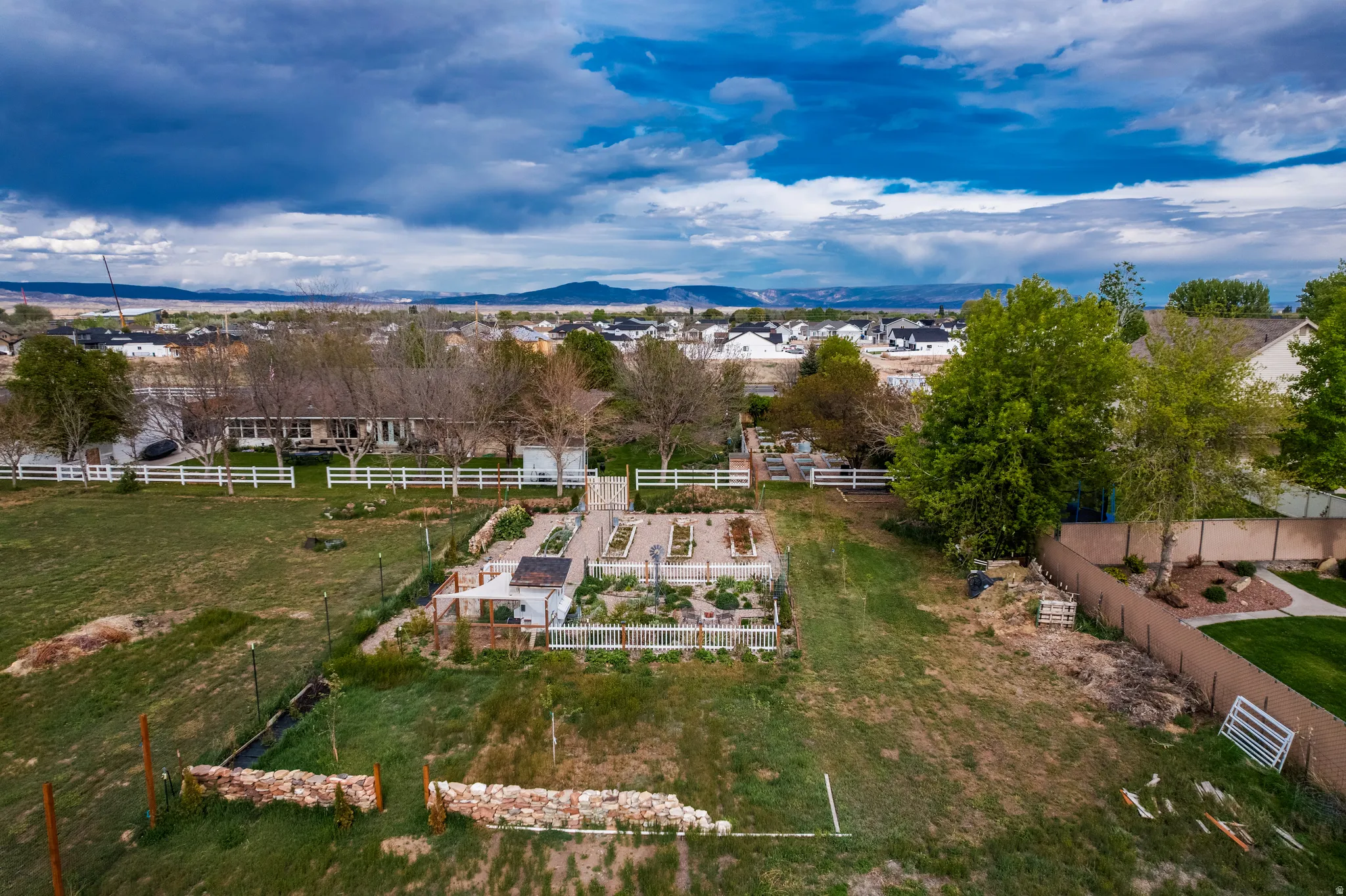 Expansive property featuring a cultivated garden area with raised beds, white picket fencing, and mature trees