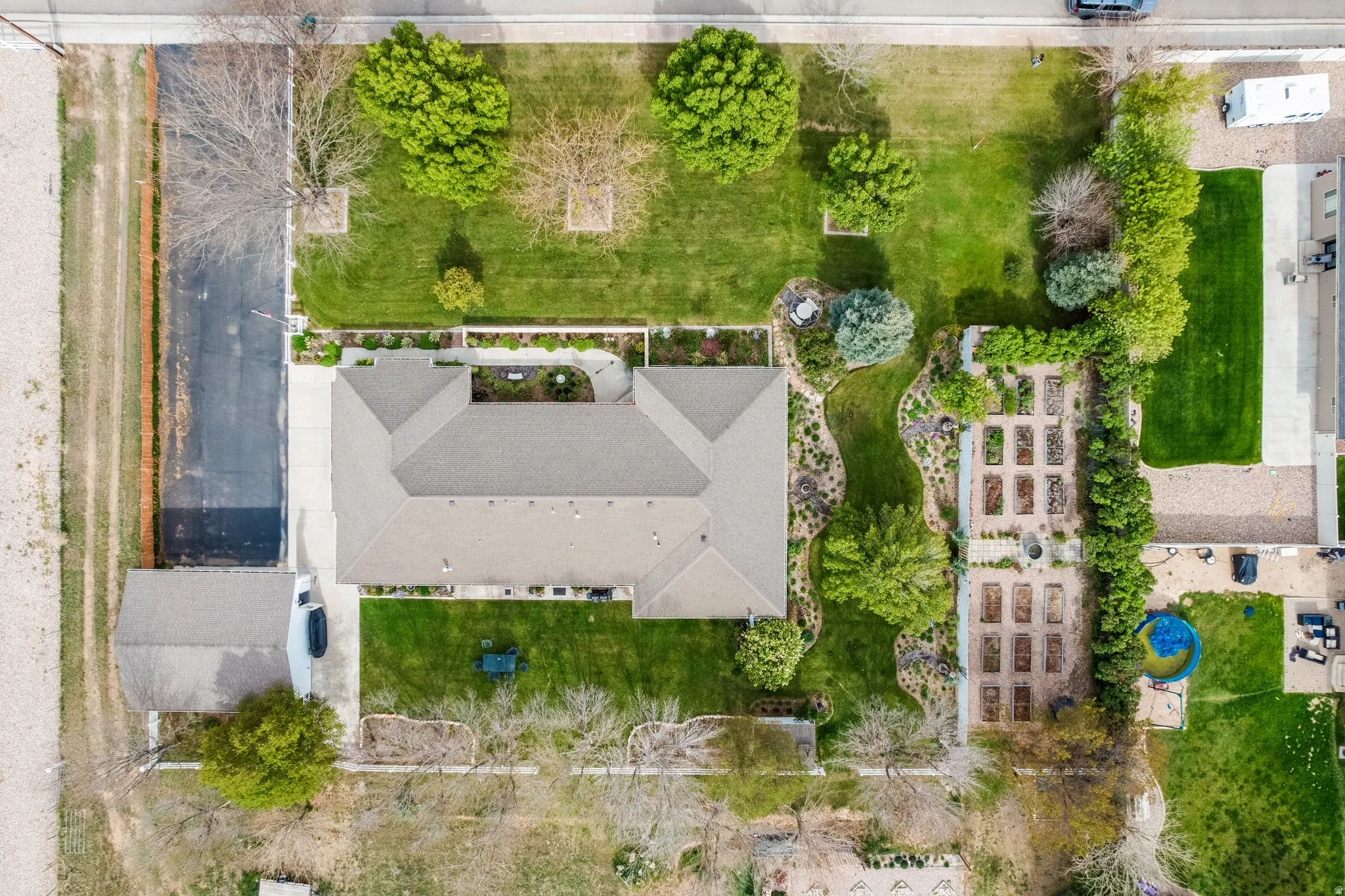 Expansive property featuring a central residence with a gabled roofline, multiple landscaped lawn areas, mature trees, a dedicated garden with organized planting beds, and a detached structure