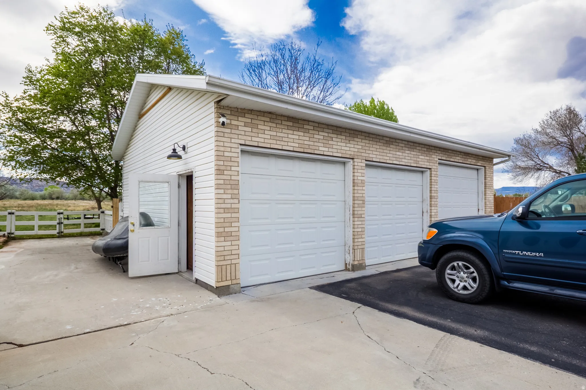 Detached garage featuring three individual bay doors, brick facade, white siding, and a side access door