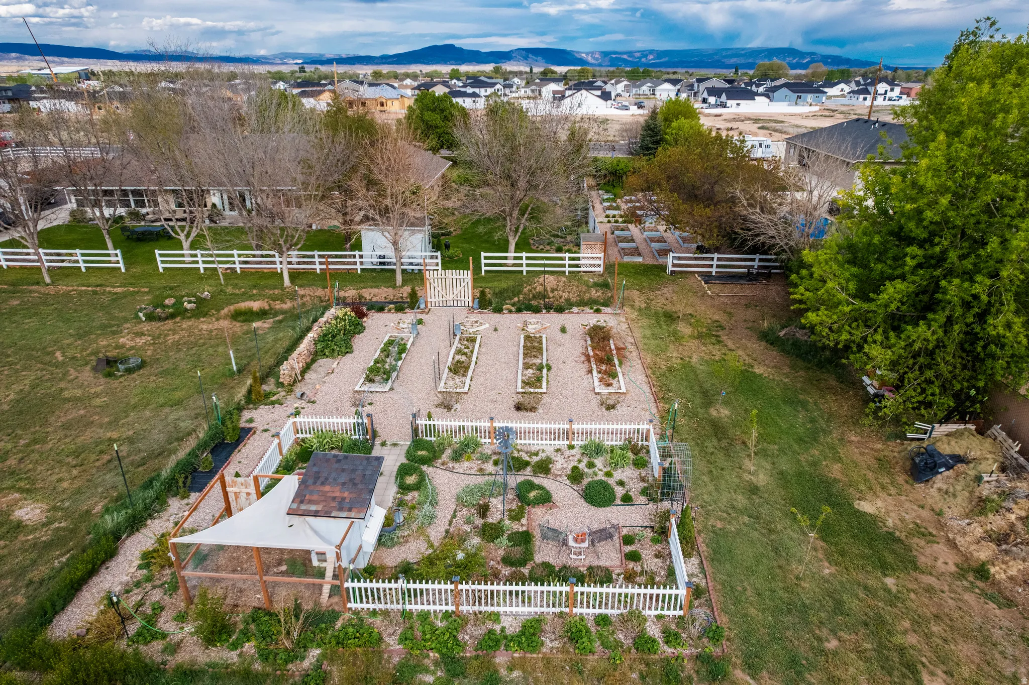 Expansive backyard featuring a fenced garden area with multiple raised beds, gravel pathways, and additional planted sections