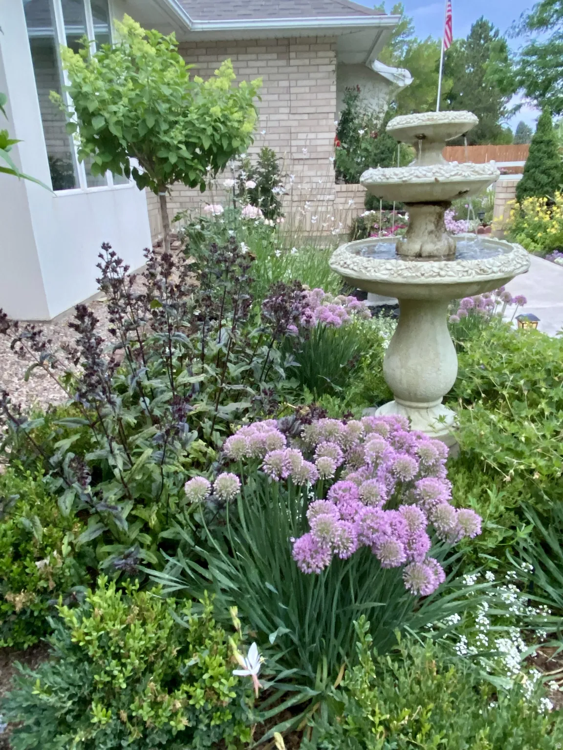 Garden area featuring a three-tiered fountain, brick exterior, and a variety of mature plantings including flowering shrubs and ground cover