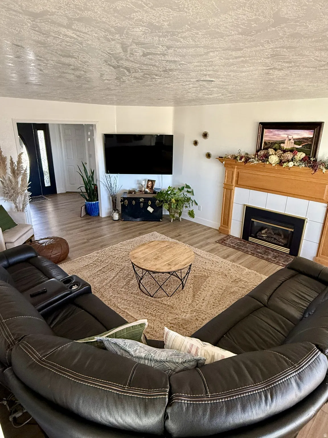Living area featuring wood-finish flooring, a fireplace with a light wood mantel and white tile surround, and an entry door with a frosted glass insert