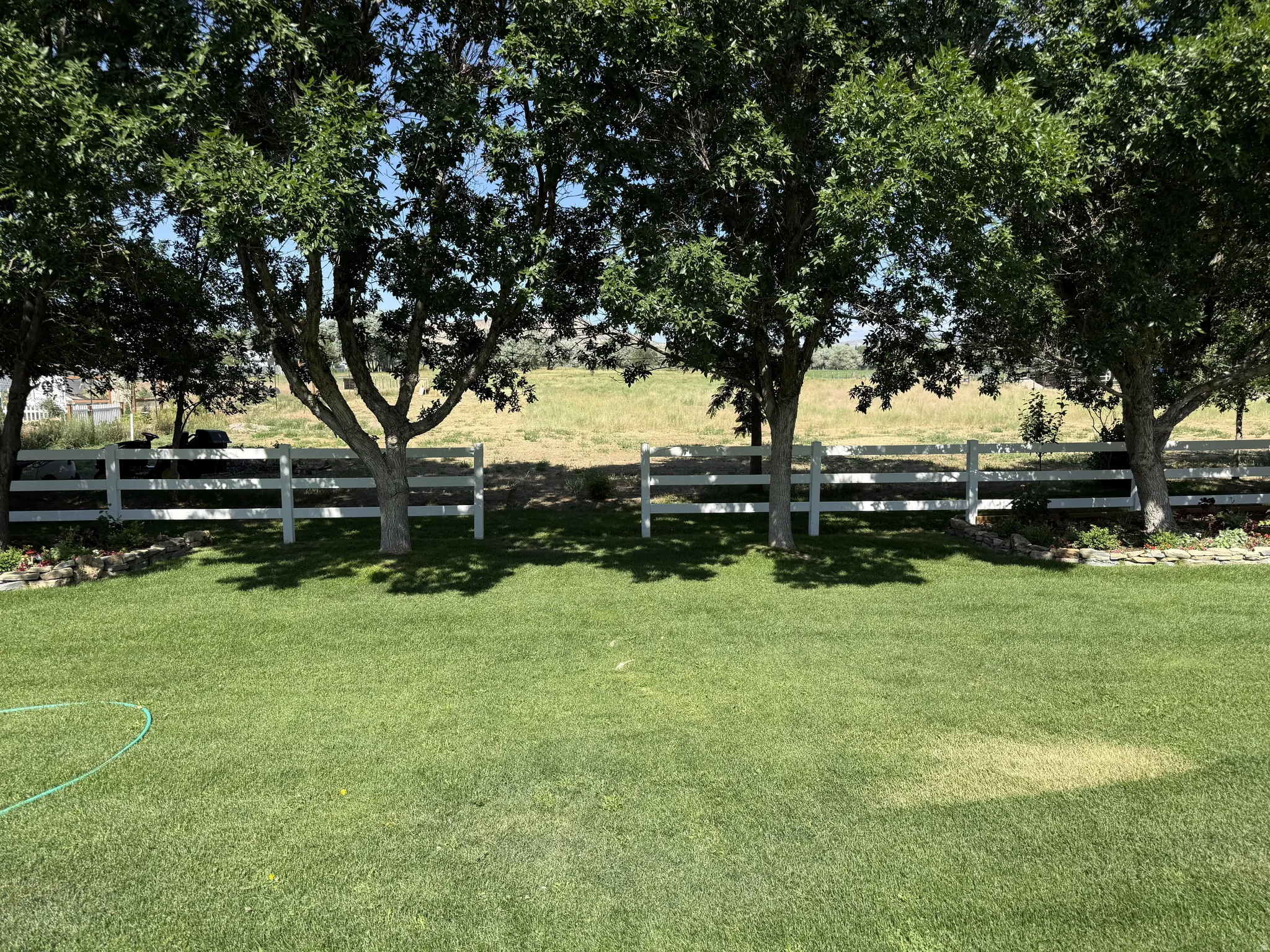 Expansive lawn area featuring mature trees and a white three-rail fence
