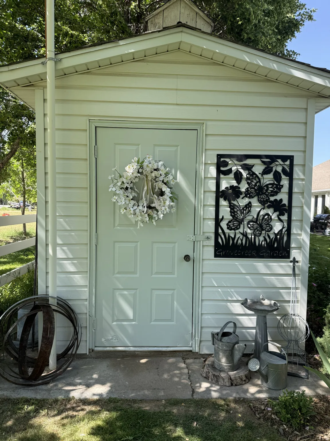 White vinyl-sided shed with a four-panel entry door, a cupola roof feature, and a concrete pad