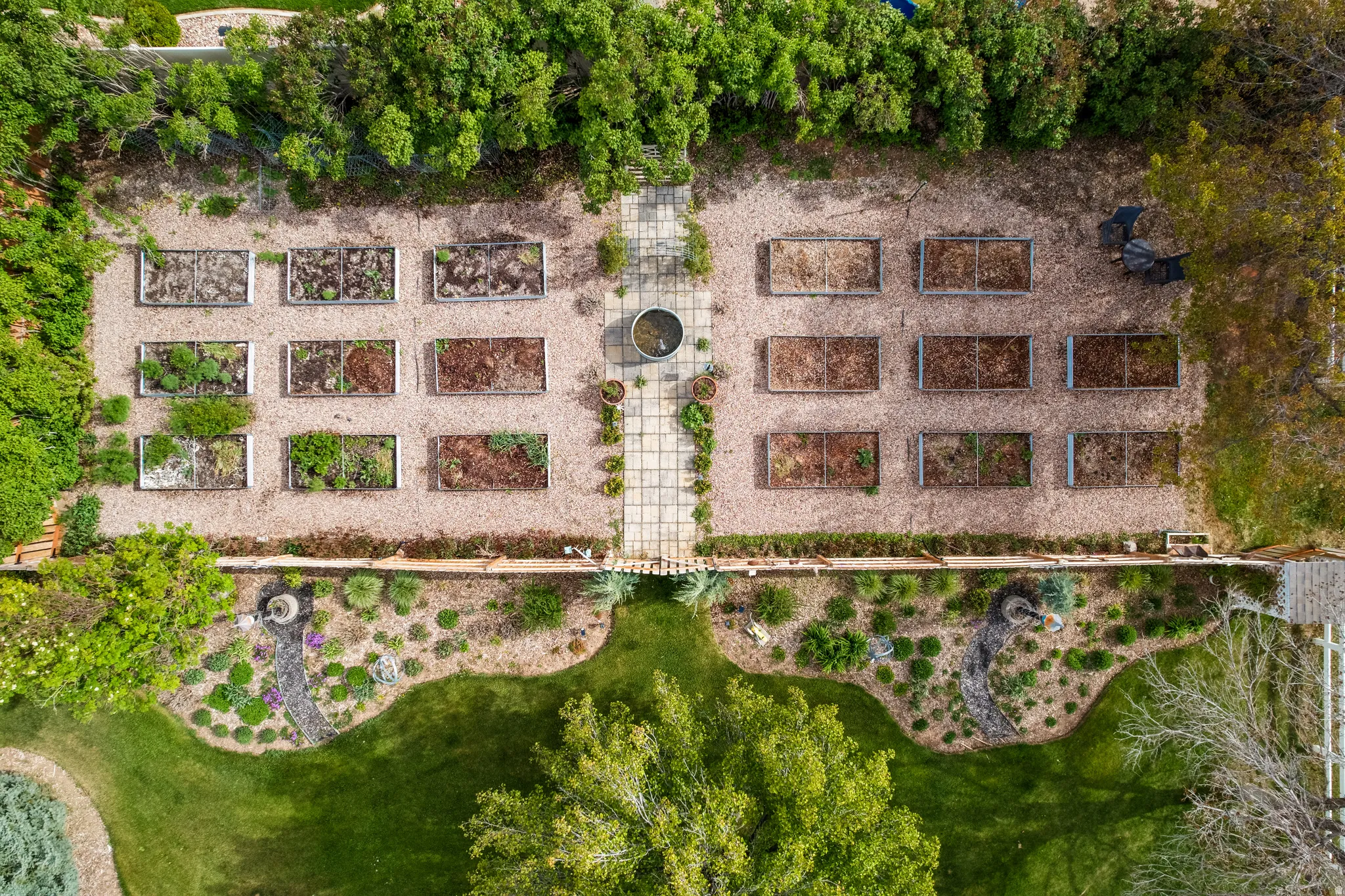 Expansive garden area featuring multiple raised beds, a central stone-paved pathway, and surrounding gravel landscaping