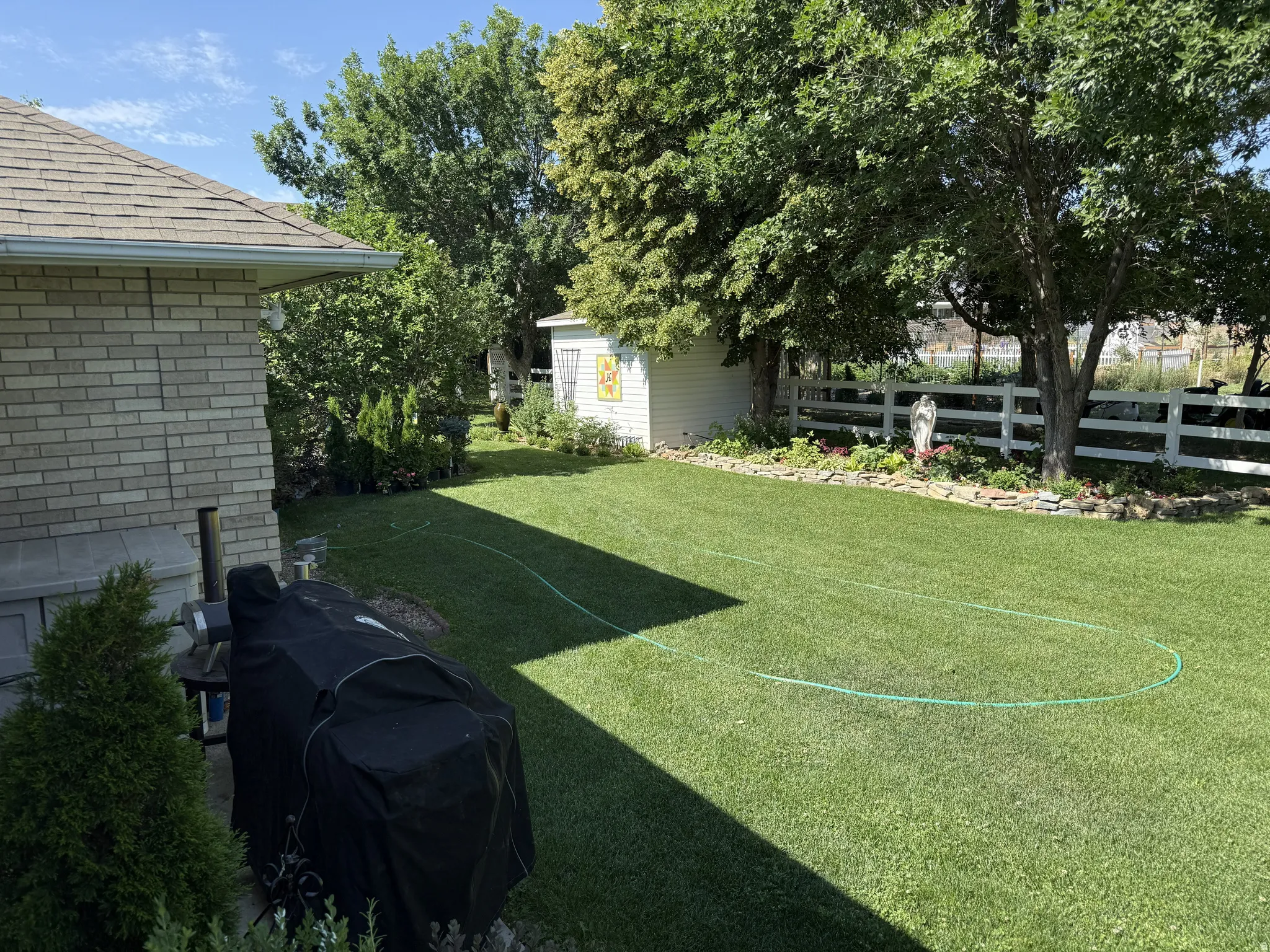 Spacious backyard with mature trees, a white picket fence, a garden shed, and a brick exterior building