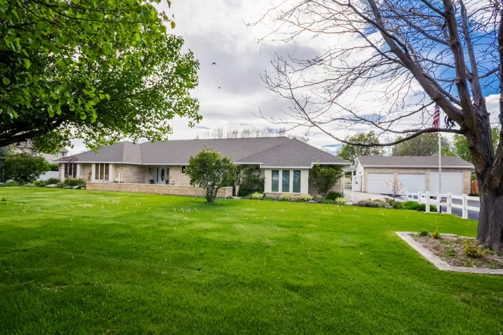 Expansive front lawn with mature trees and a long driveway leading to a three-car garage