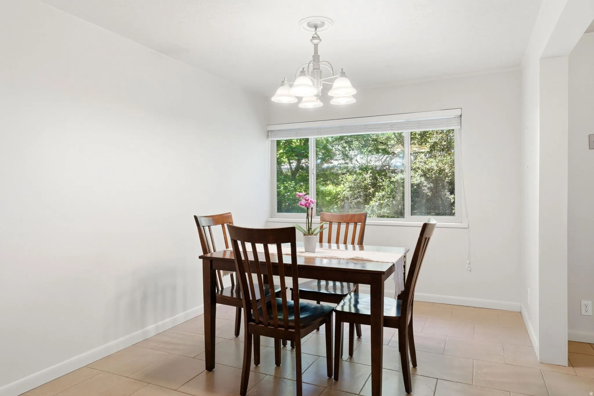 Dining area featuring a large window, tiled flooring, an overhead chandelier, and white walls
