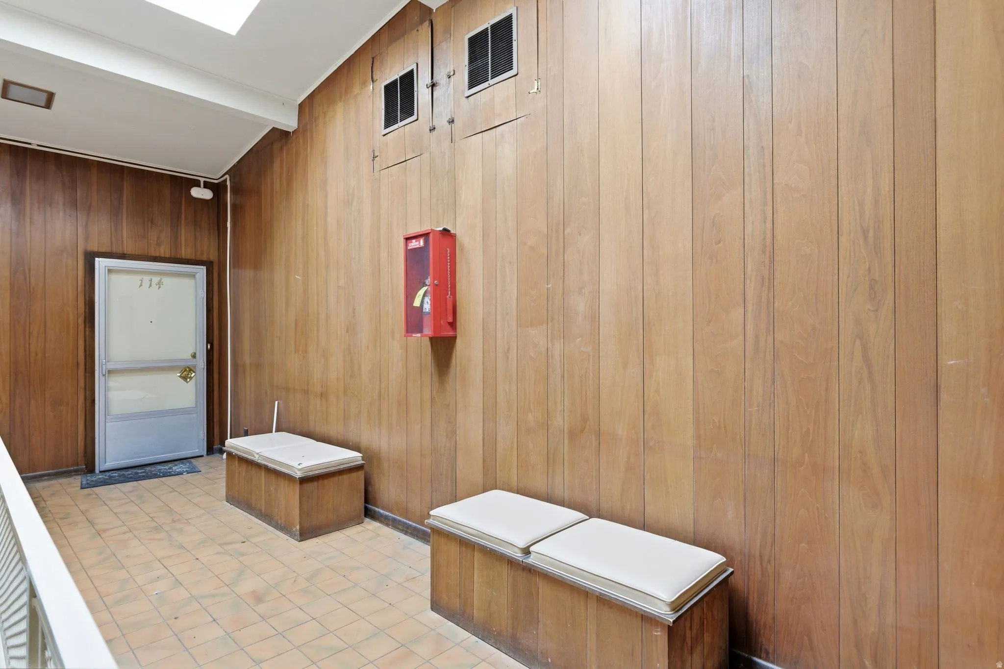 Entryway featuring wood paneling, tiled flooring, an overhead skylight, and built-in benches with light-toned cushions