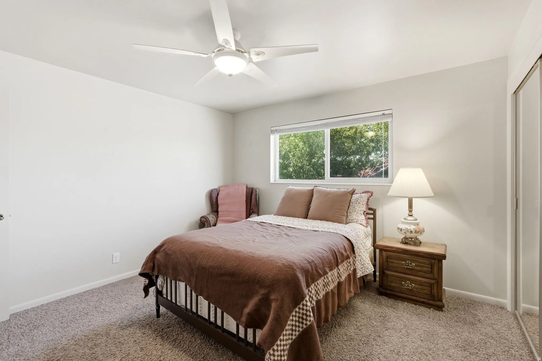 Bedroom featuring a ceiling fan, carpet flooring, a window providing natural light, and a built-in closet with sliding doors