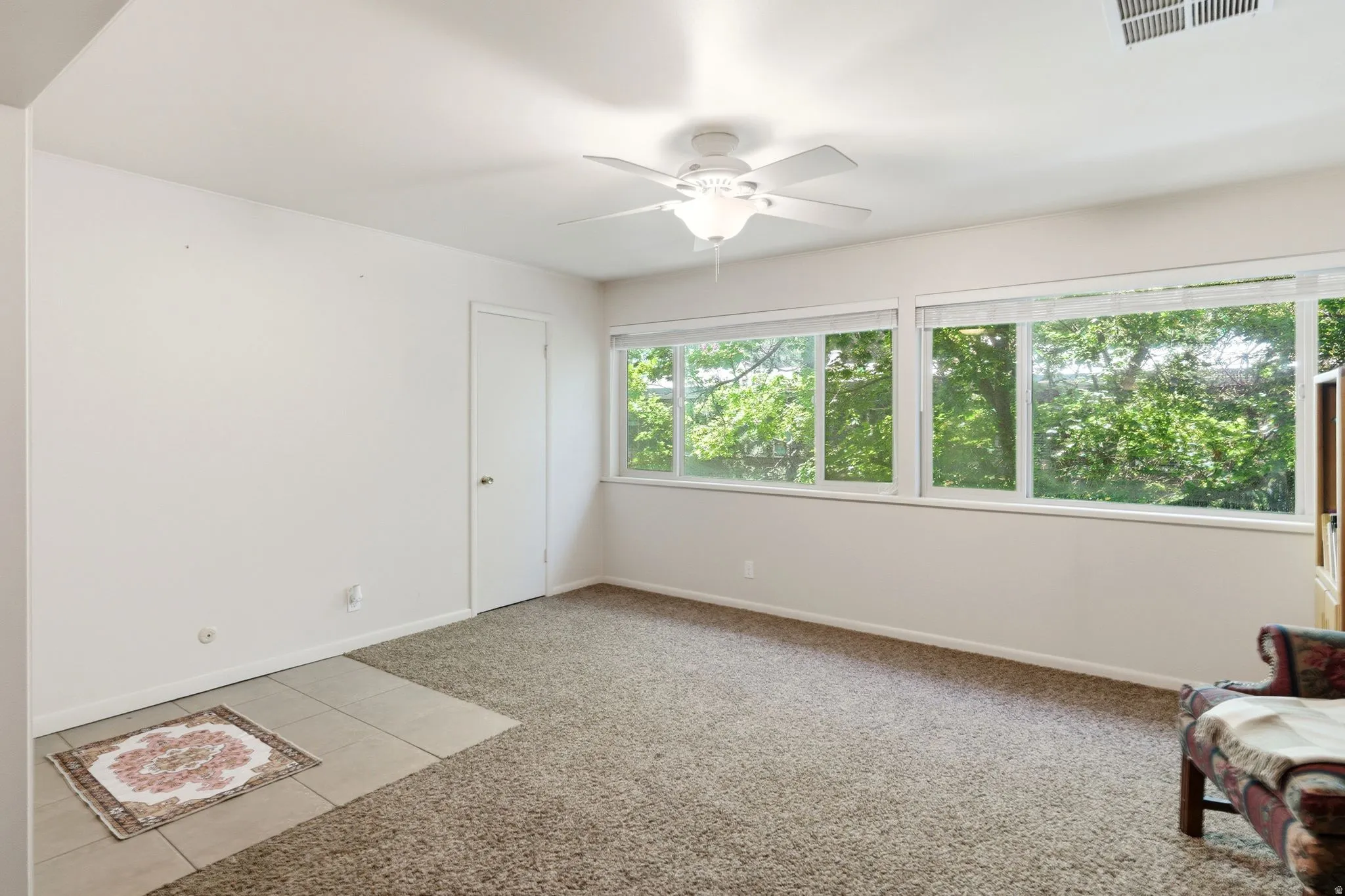 Carpeted room featuring a ceiling fan with integrated lighting, multiple windows with natural light, and a white interior door