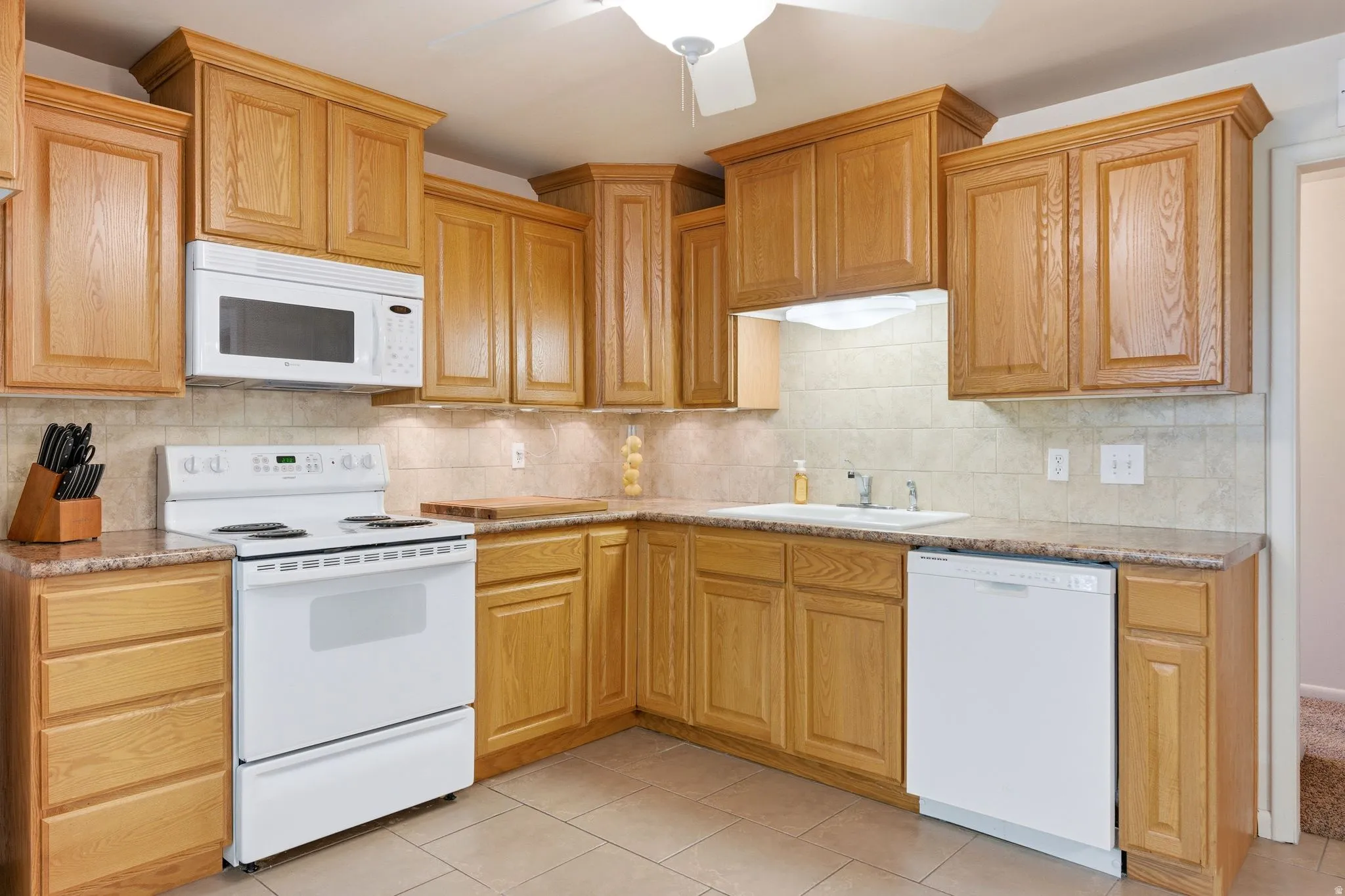 Kitchen featuring light wood cabinetry, white appliances, and a tile backsplash