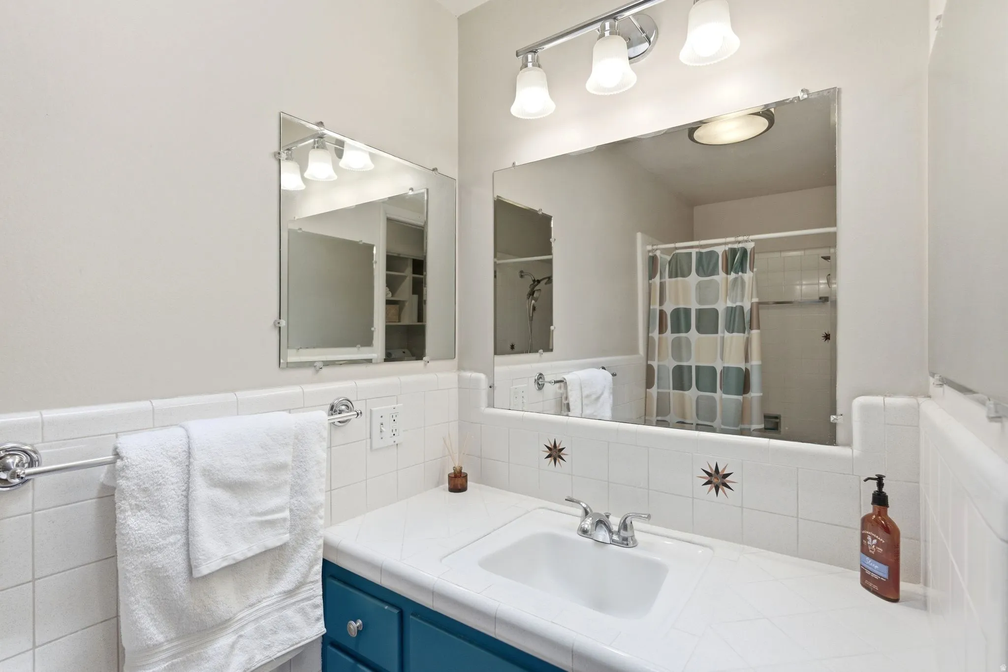 Bathroom featuring a white tile countertop, integrated rectangular sink, chrome-finish faucet, and a teal-painted vanity with chrome hardware
