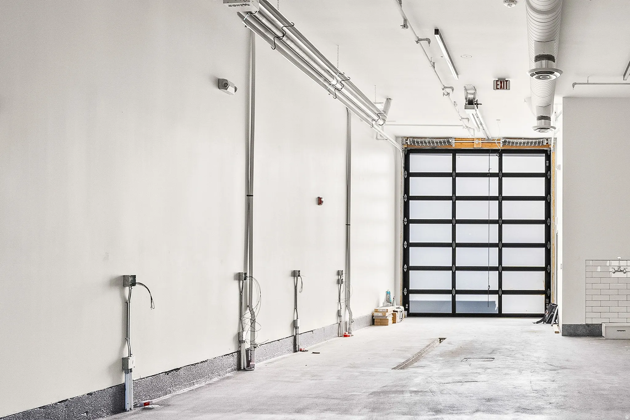Interior commercial space featuring a full-light overhead door, exposed ceiling ductwork, and track lighting