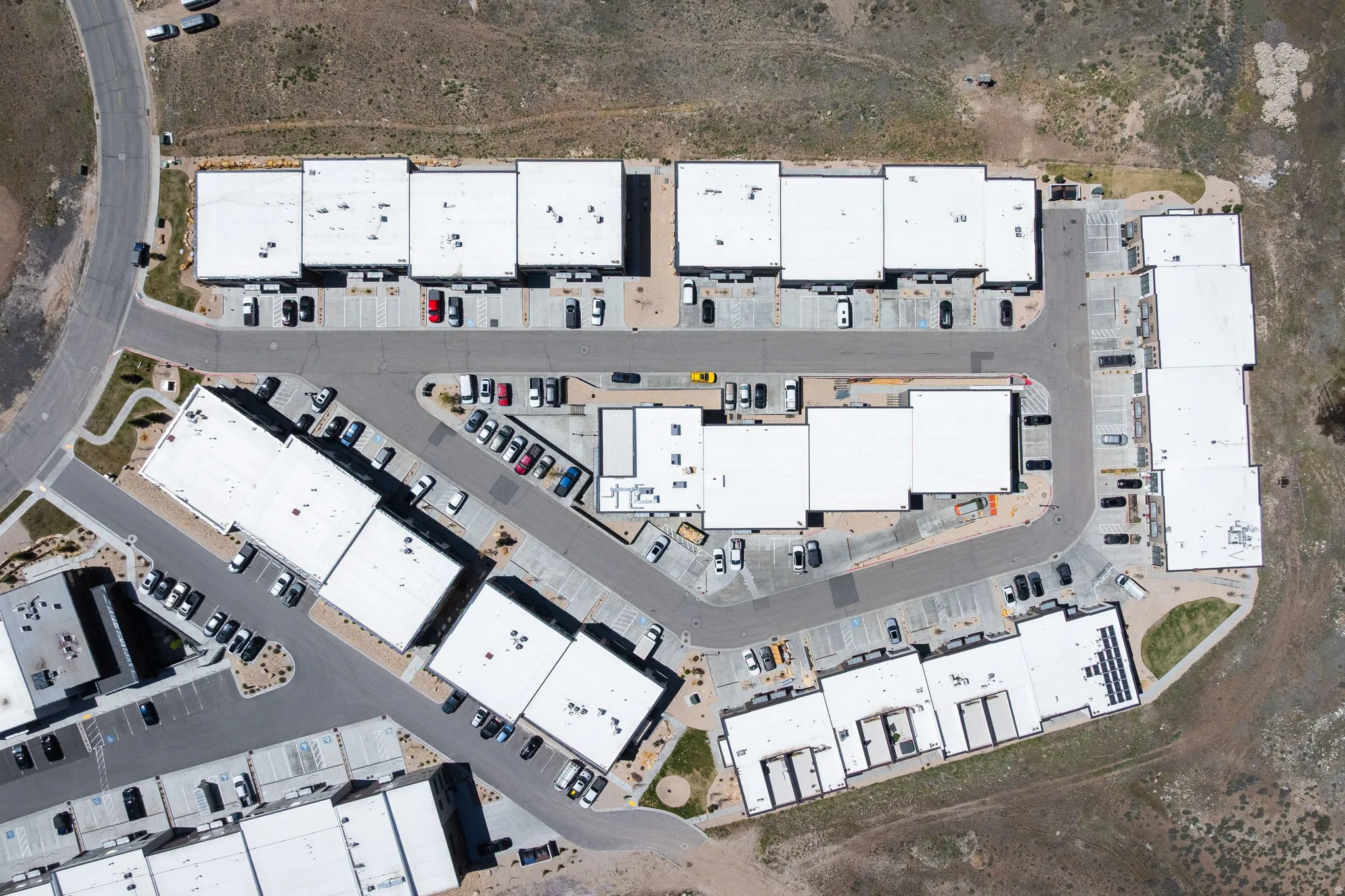 Aerial view of a commercial complex featuring multiple buildings with white flat roofs and integrated parking areas