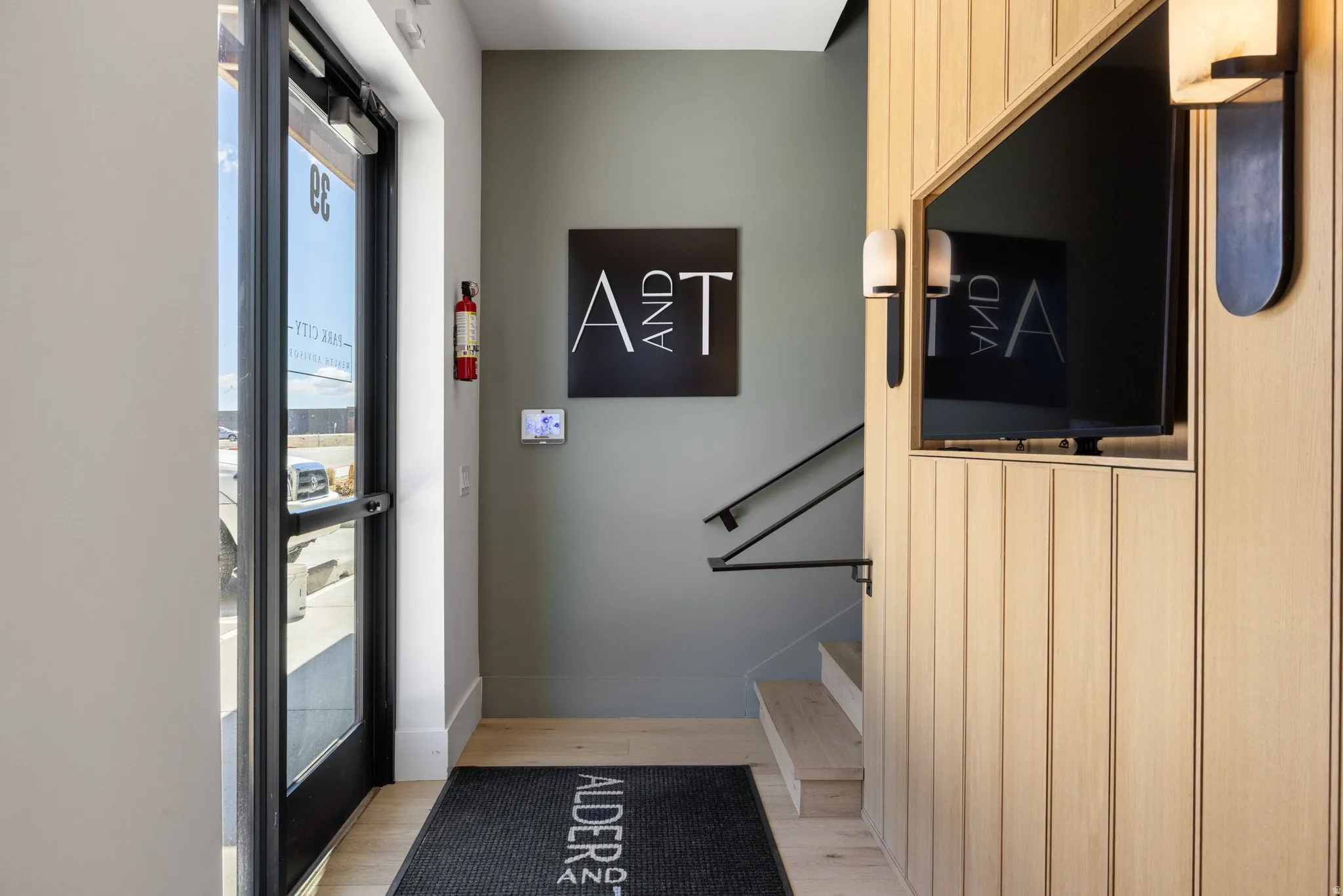 Entryway featuring vertical wood paneling, contemporary wall sconces, wood-finish flooring, and a black metal handrail leading to a lower level
