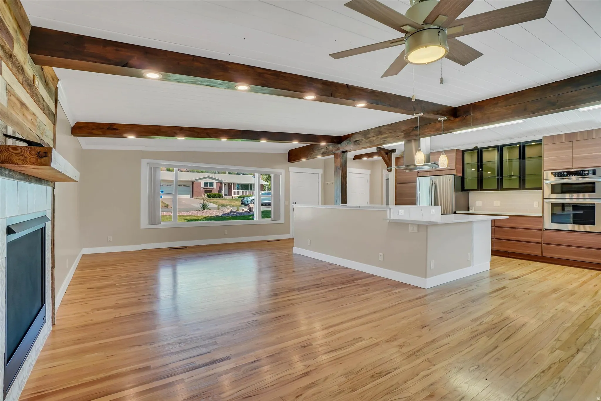 Open-concept living space featuring wood-finish flooring, exposed ceiling beams with recessed lighting, and a modern ceiling fan