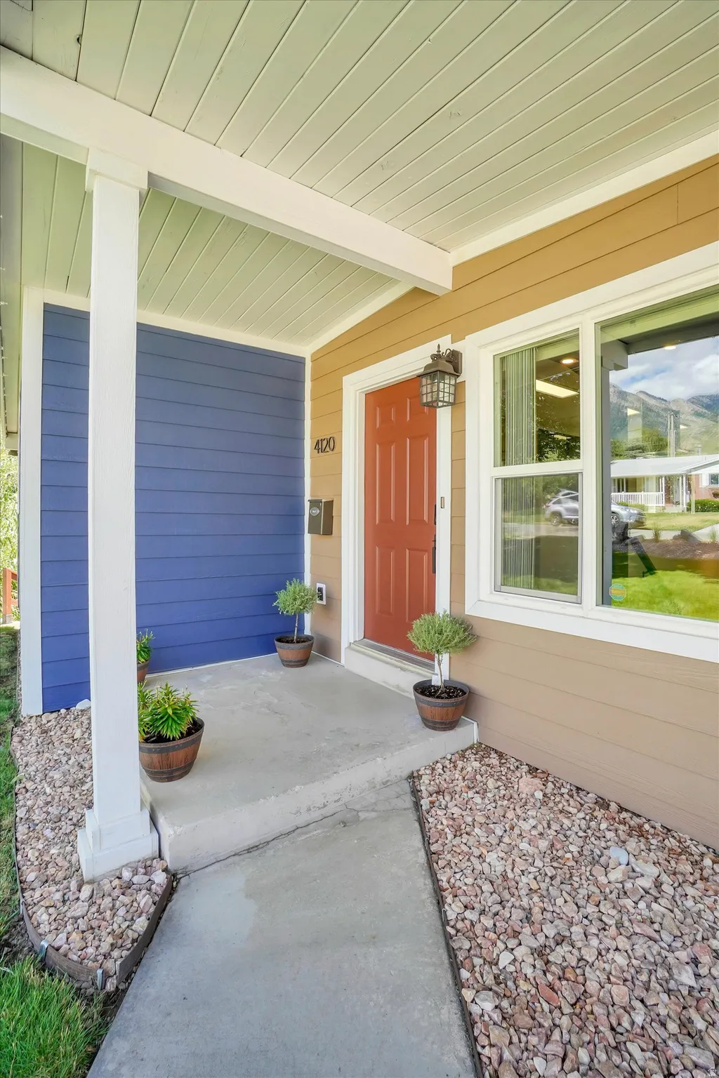 Covered porch entry featuring a red paneled door, exterior wall lantern, and concrete walkway