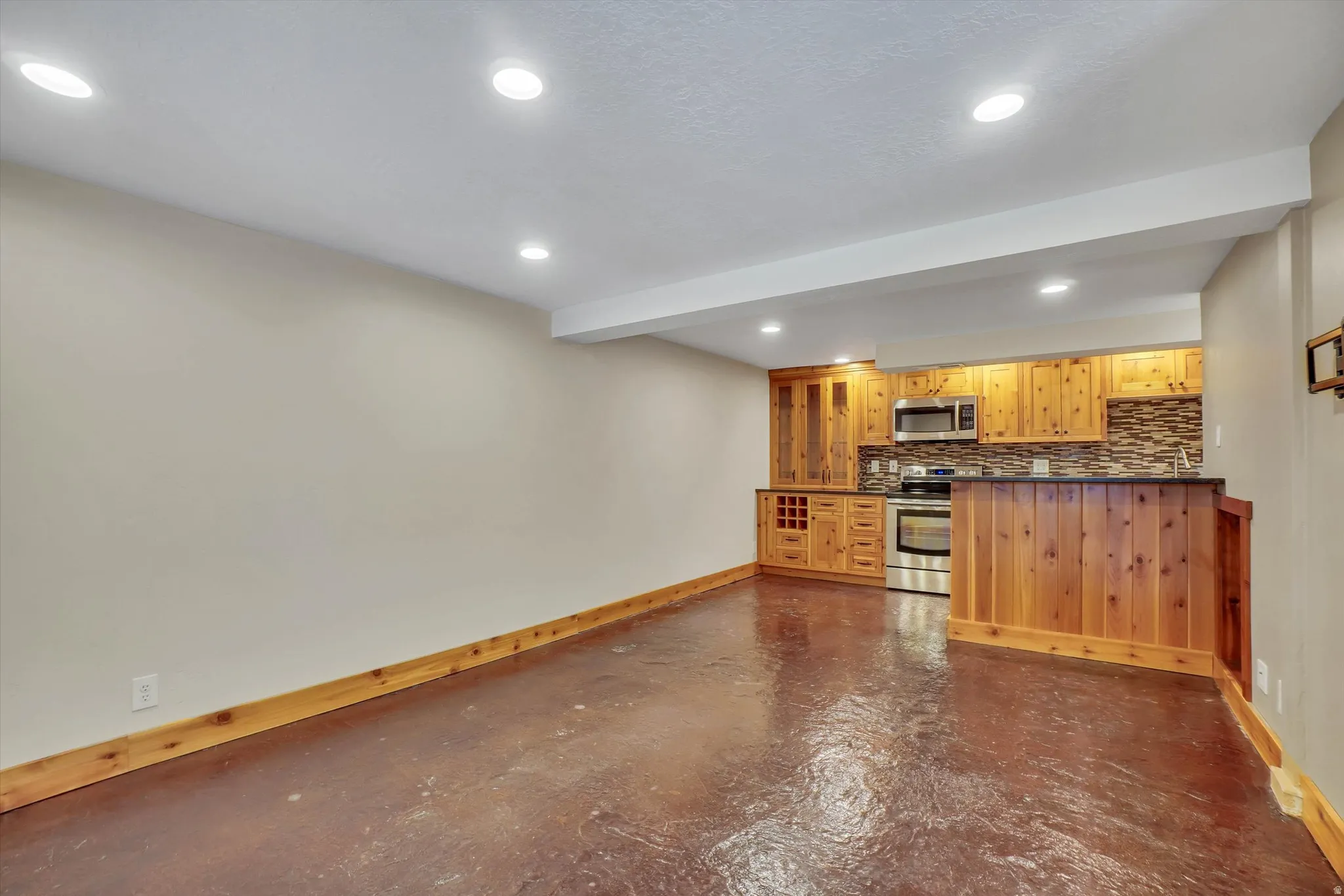 Compact kitchen area featuring wood-finish cabinetry, stainless steel appliances, a tile backsplash, and a breakfast bar