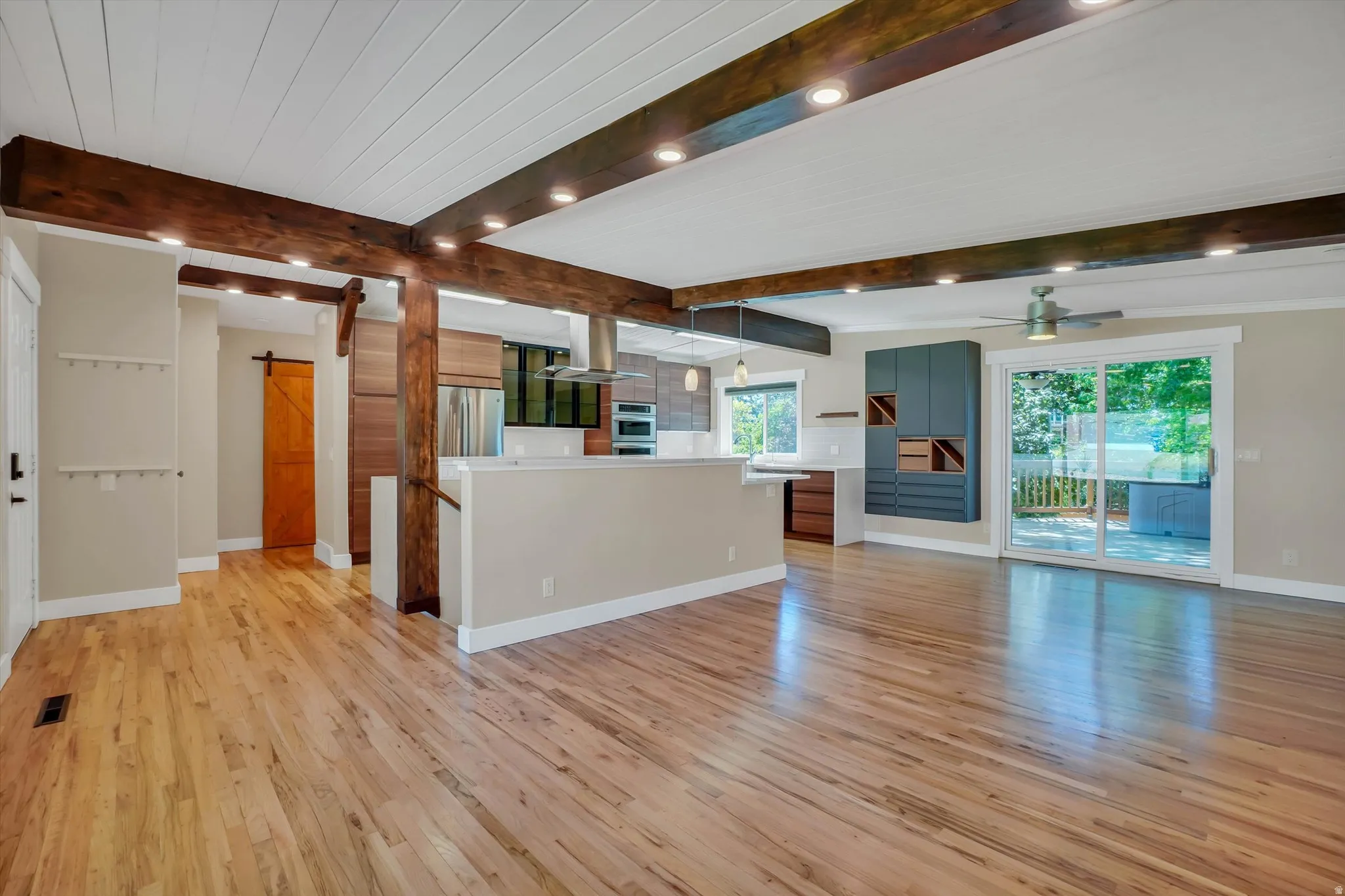 Spacious open-concept living area featuring wood-finish flooring, exposed ceiling beams with recessed lighting, and a white planked ceiling