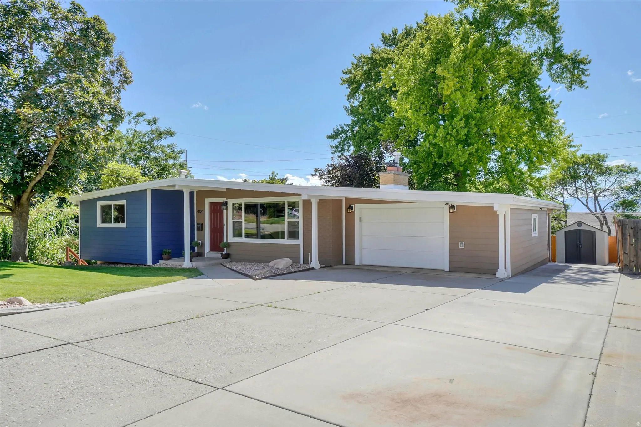 Modern ranch-style home featuring a two-tone facade, attached garage with white door, covered entry, and expansive concrete driveway