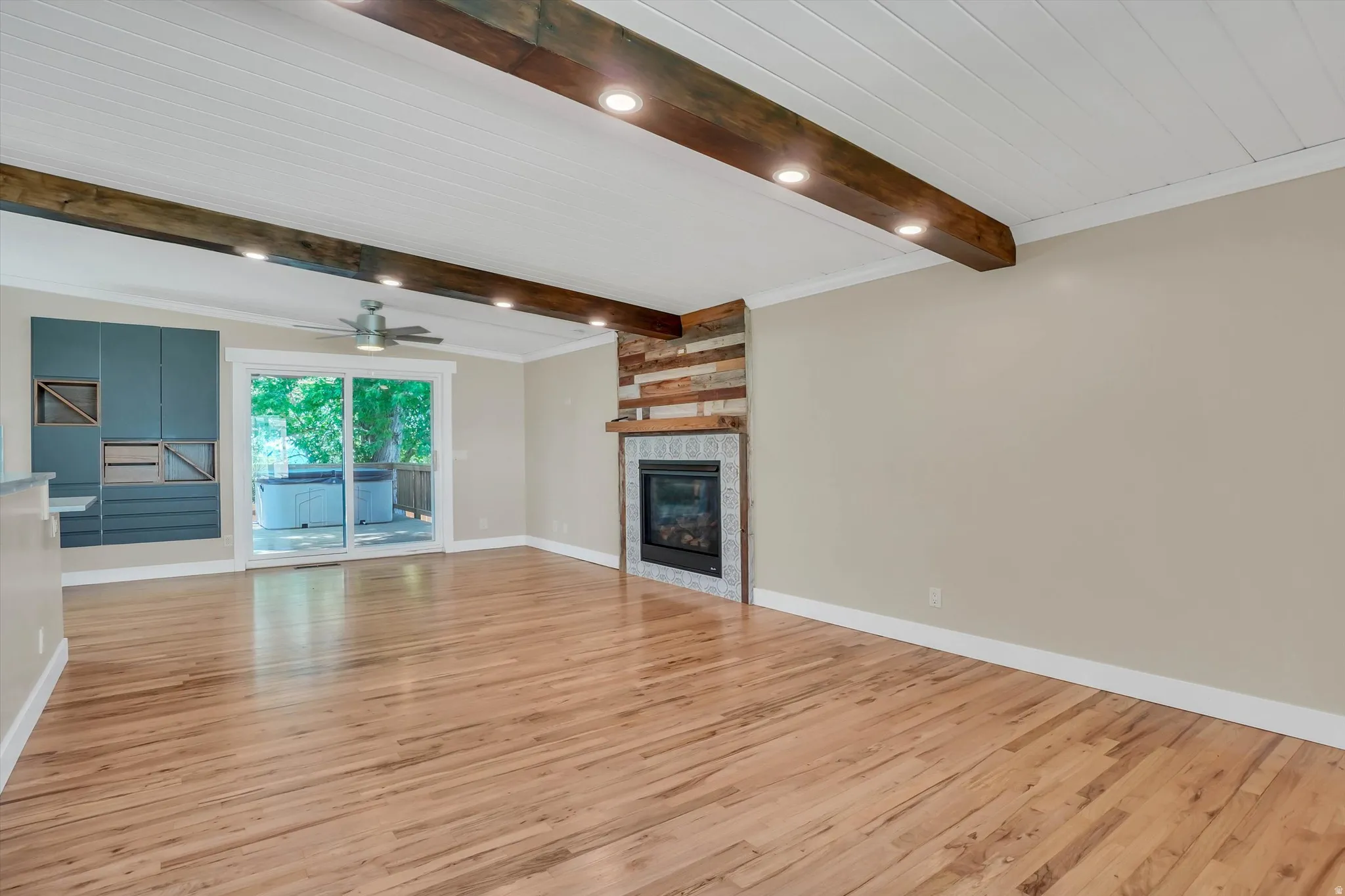 Spacious room featuring wood-finish flooring, a contemporary fireplace with a wood mantle, and exposed ceiling beams with recessed lighting