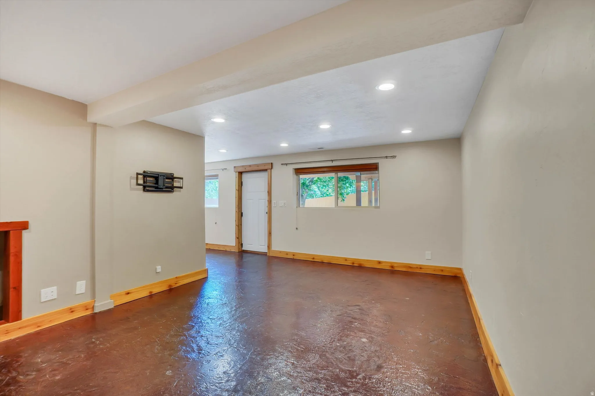 Spacious room featuring durable concrete flooring, recessed lighting, white trim, and a built-in television mount